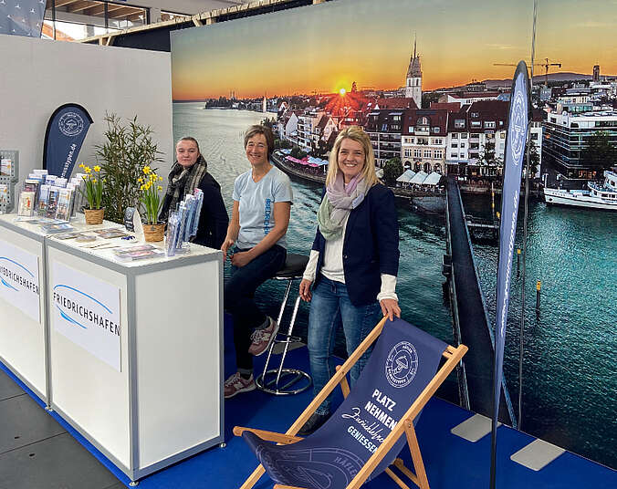Drei Frauen hinter einem Tresen am Stand, im Hintergrund Foto von Friedrichshafen