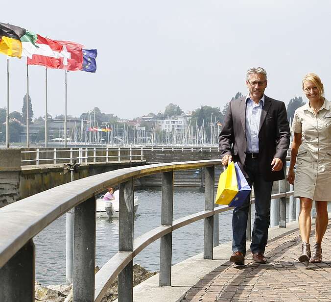 Vier Personen mit Einkaufstaschen laufen auf der Uferpromenade